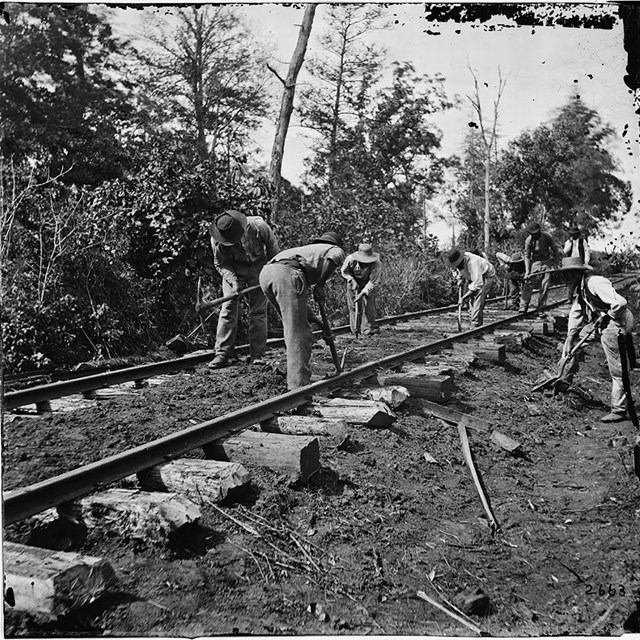 African American men dig along a railroad track.