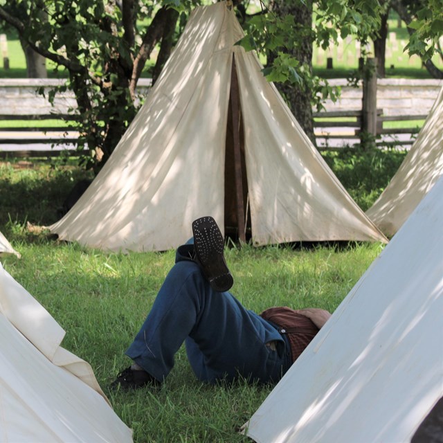 A Union Soldier laying down among white canvas tents.