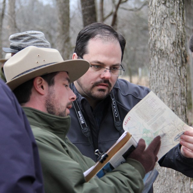 A ranger points to a map while visitors look on.