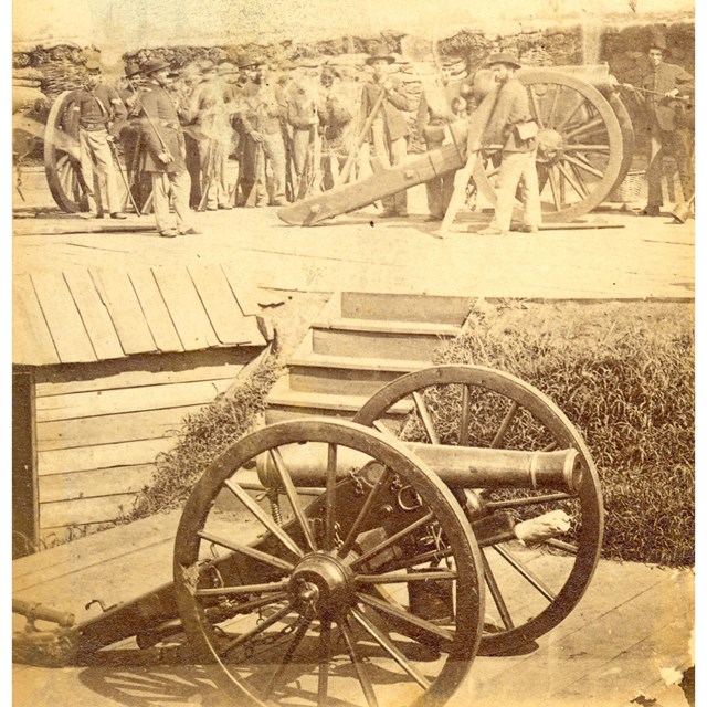 A black and white photo of a cannon on a wooden platform, with soldiers and another cannon on a plat
