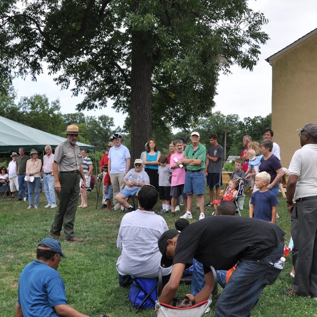 A group of people stand around a park ranger who is talking to the crowd. 