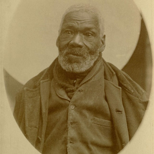 An older Black man sitting for a photo.