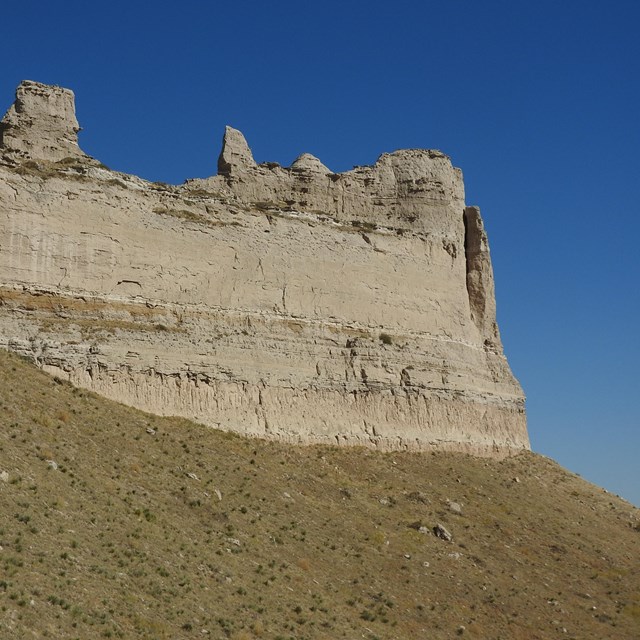 A large sandstone formation below which can be seen scattered boulders. 