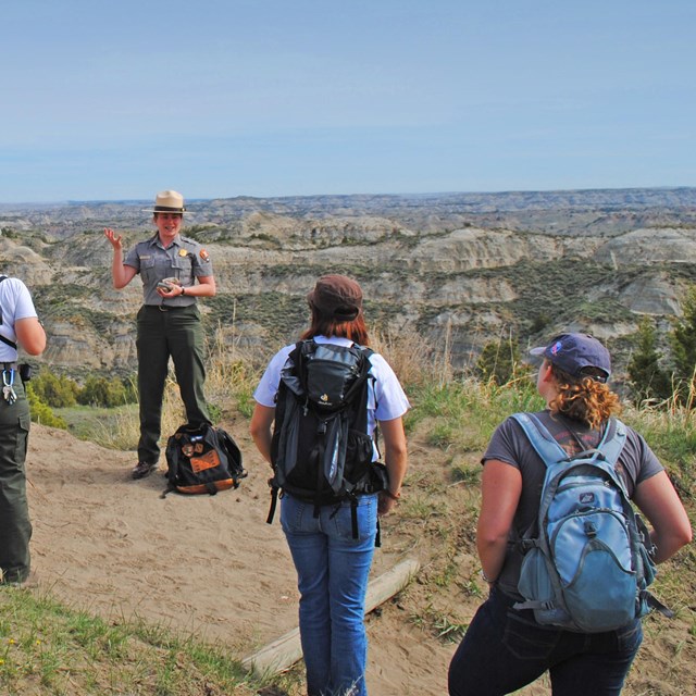 A ranger and group of park visitors standing along a trail on a grassy ridge.