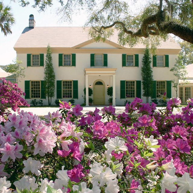 a historic club white with green shutters and bright flowers in the foreground 