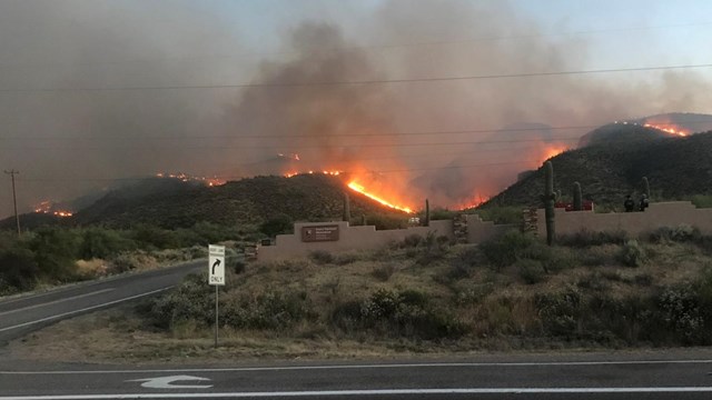 Wildfire rises over desert mountains above a highway