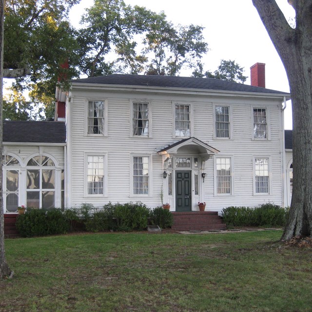 large white house with green grass in front and trees left and right