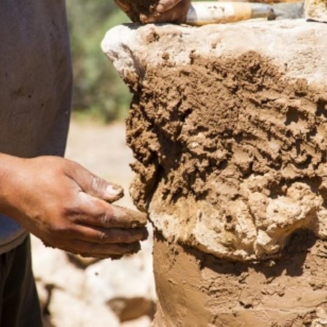 Close up photo of a hand applying clay to an exterior wall.