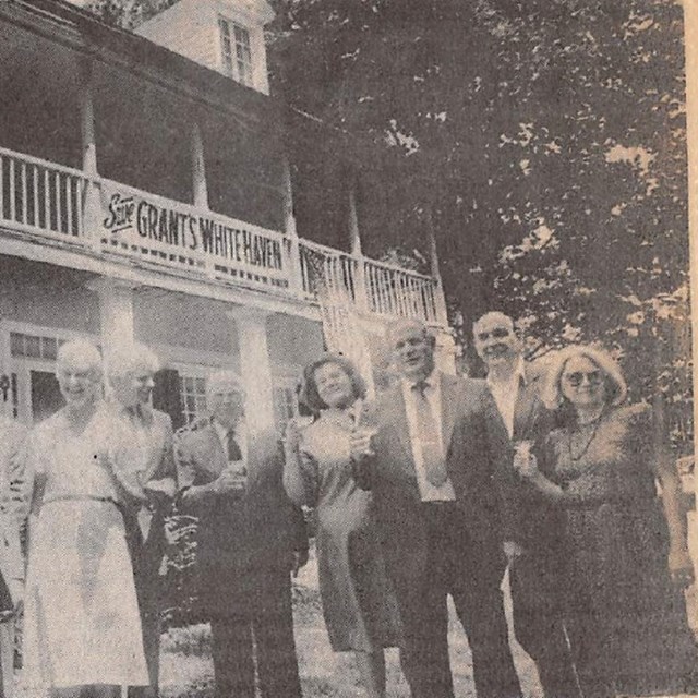 Group of people holding wine glasses and having a toast in front of a house.