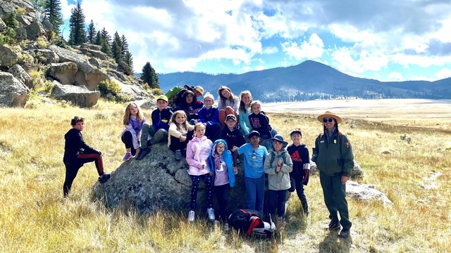 A park ranger and a group of children pause for a photo during a guided hike in a grassland.