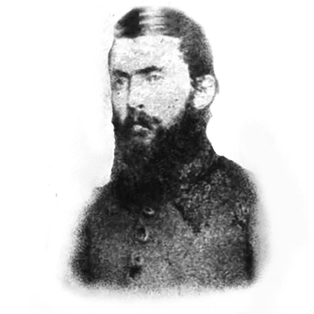 A black and white image of a man with full, dark beard and parted hair. 