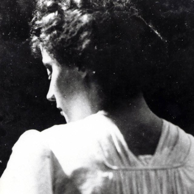 A black and white image of a women wearing a white dress with her back facing the camera.