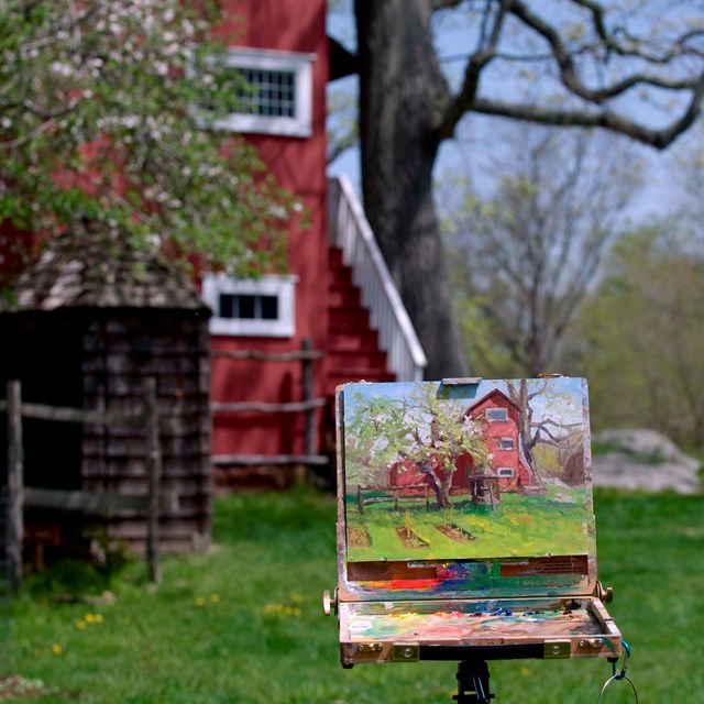 An easel with a painting of a historic building set up outside, with the building in the background