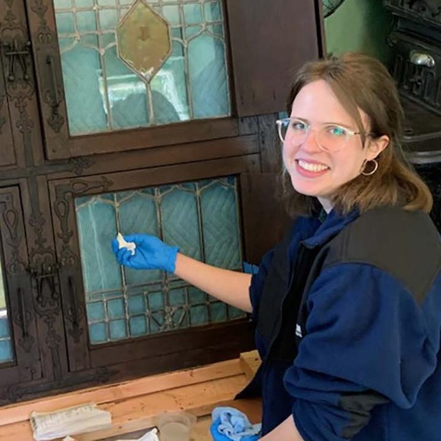 A person wearing blue gloves holds a swab to glass windows on the ground