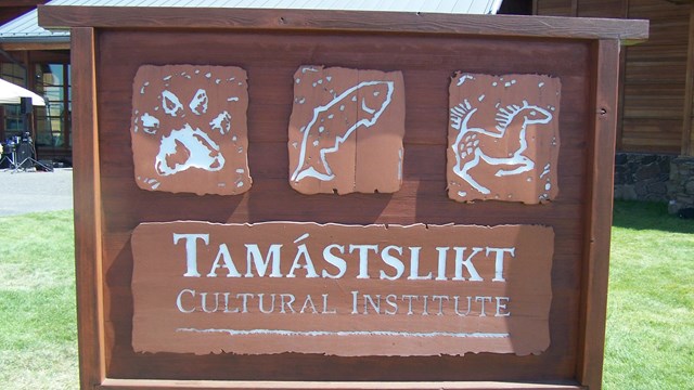 vertical wooden sign "Tamastslikt Cultural Institute" with 3 drawings: a paw print, fish, and horse 