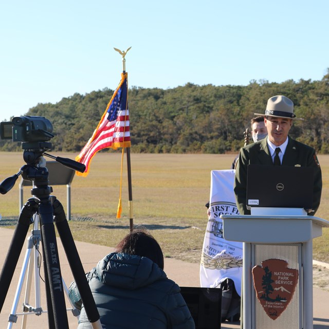 Park ranger at a podium with a news camera in front