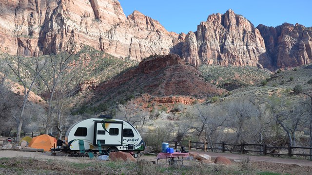 A camping trailer sits in a campground, with red cliffs in the background