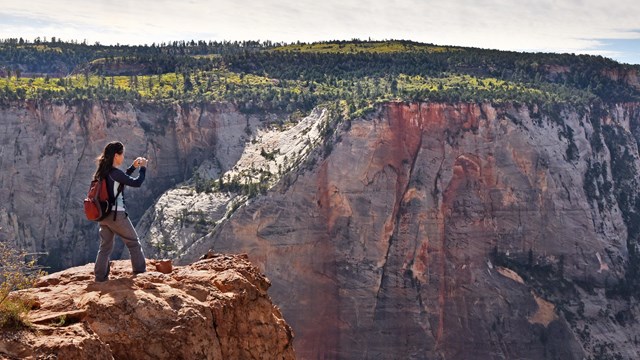 A hiker takes a picture overlooking steep cliffs