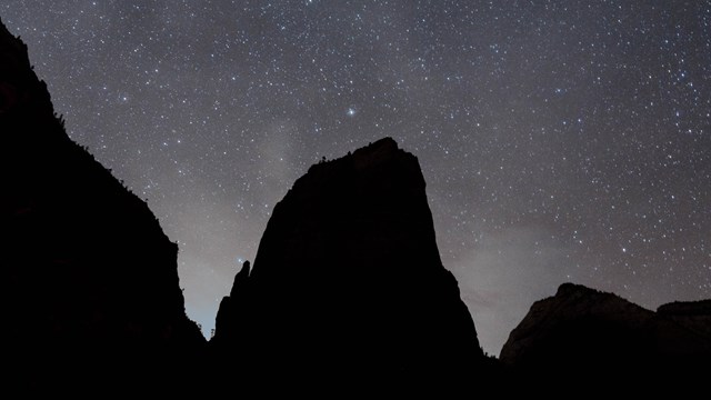 Large cliffs are silhouetted against a starry night sky
