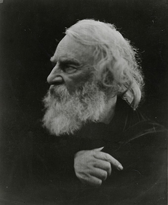 Black and white portrait of Henry Longfellow with white hair and beard in profile wearing black cape