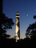 Cape Lookout Lighthouse illuminated with quarter moon in the night sky.