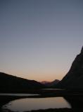 Evening light reflects in a completely calm lake surrounded by jagged mountains.