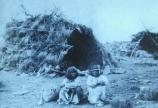 Two Paiute outside of their hogan in a village setting