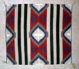 Navajo Rug, Third Phase Chief design. Colors are primarilly red, blue, white, and gray. Often square. Triangles in the corners and a diamond in the center. Striped without a border.
