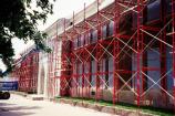 Scaffolding is in place to allow workers access while re-pointing the brick. Old mortar is removed and then new, red mortar is added.