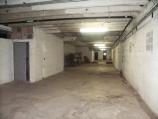 Large, long room with concrete walls. There's an old laundry press on the left in the background. You can see through another room to a side exterior door.
