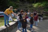 Ladies standing on a low rock retaining wall hand white plastic bags stuffed with souvenirs to young school children.