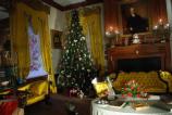 View of the music room decorated for yuletide. Christmas tree festooned with period appropriate ornaments.