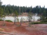 Steam rises on the lake surrounded by red thermally altered soil.