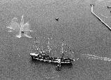 Photo taken from a helicopter looking down on a 19th century sailing vessel being pushed by a tugboat.