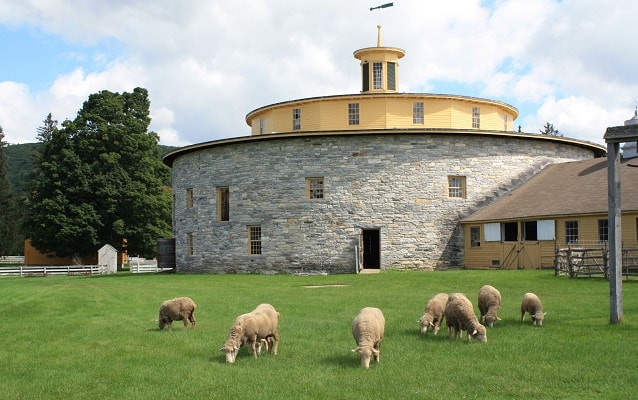 sheep grazing in front of a circular, stone barn