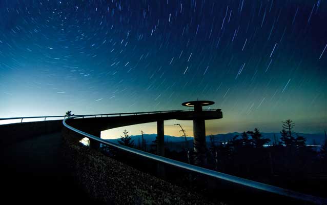 evening photo of ramp up to clingmans dome observation tower with stars above, mountains in distance