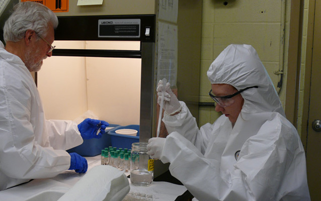 Two staff wearing protective clothing and glasses work in a laboratory.