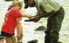 High School student hired as a park ranger helps a child find stream invertebrates in a park stream.