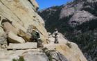 Trail crew members remove rockfall on a cliffside trail.