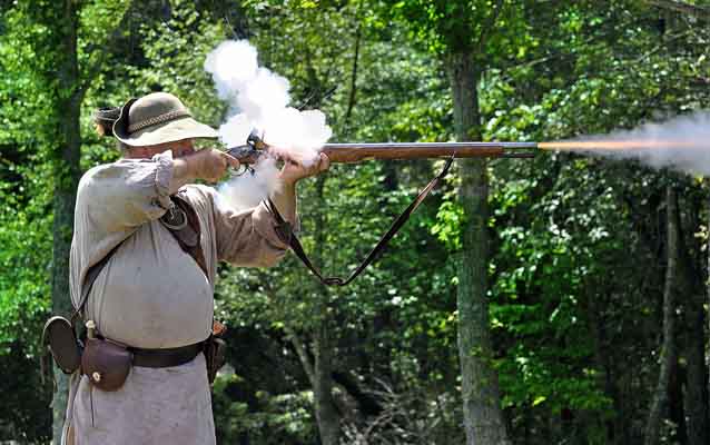 Smoke rises from the lock and fire shoots from the end of a musket as a reenactor fires.