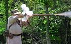 Smoke rises from the lock and fire shoots from the end of a musket as a reenactor fires.