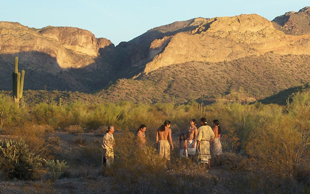 Actors in costumes from the Hohokam era stand in a circle in front of the Superstition Mountains