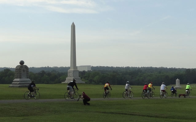 Bicycles ride past a series of stone monuments