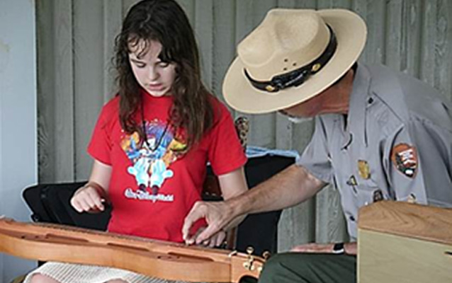A ranger helps a young girl play a lap dulcimer in a Parks As Classrooms program.