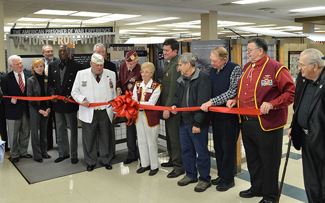 A group of people stand by exhibit panels and cut a red ribbon.