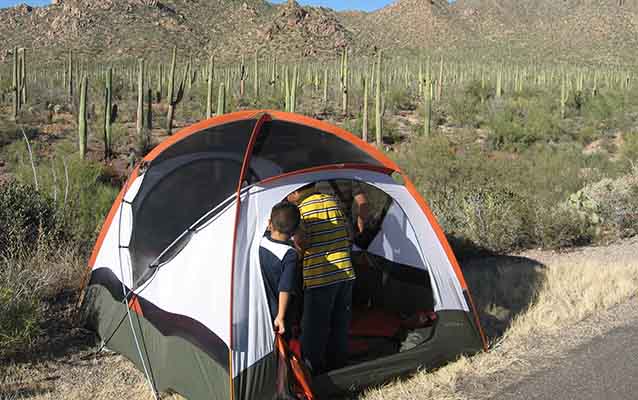Children explore a tent with a backdrop of the Sonoran Desert behind the tent .