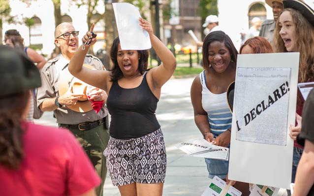 A group of teens sing on Independence Square, with one girl holding papers above her head while another holds a poster with the words