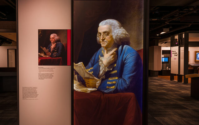 Benjamin Franklin Museum exhibit panel featuring Franklin's image in the foreground; museum in the background.