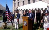 Surrounded by soldiers and American flags, Senator Gillibrand and Brand USA's Mike Fullerton present at a podium in front of an old stone fort.