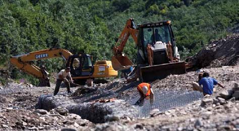 people and construction equipment working in a rocky stream bed